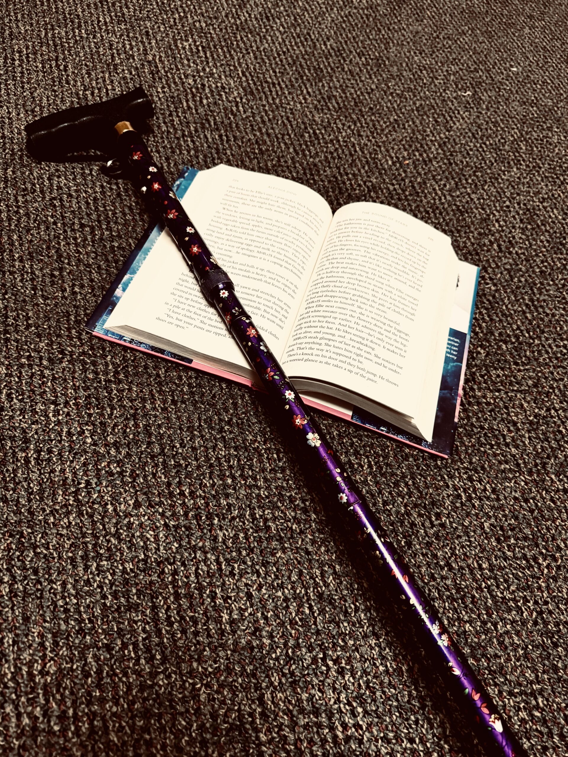 A walking cane is laid out over an open book on the floor.